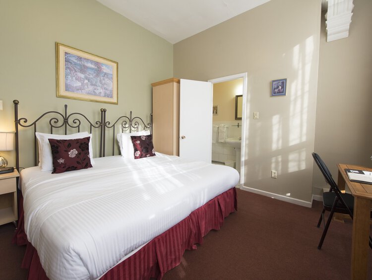 A bright guest room with a king bed, a nightstand, and a work desk