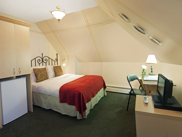 A bright guest room with a double bed, a desk, and a small TV