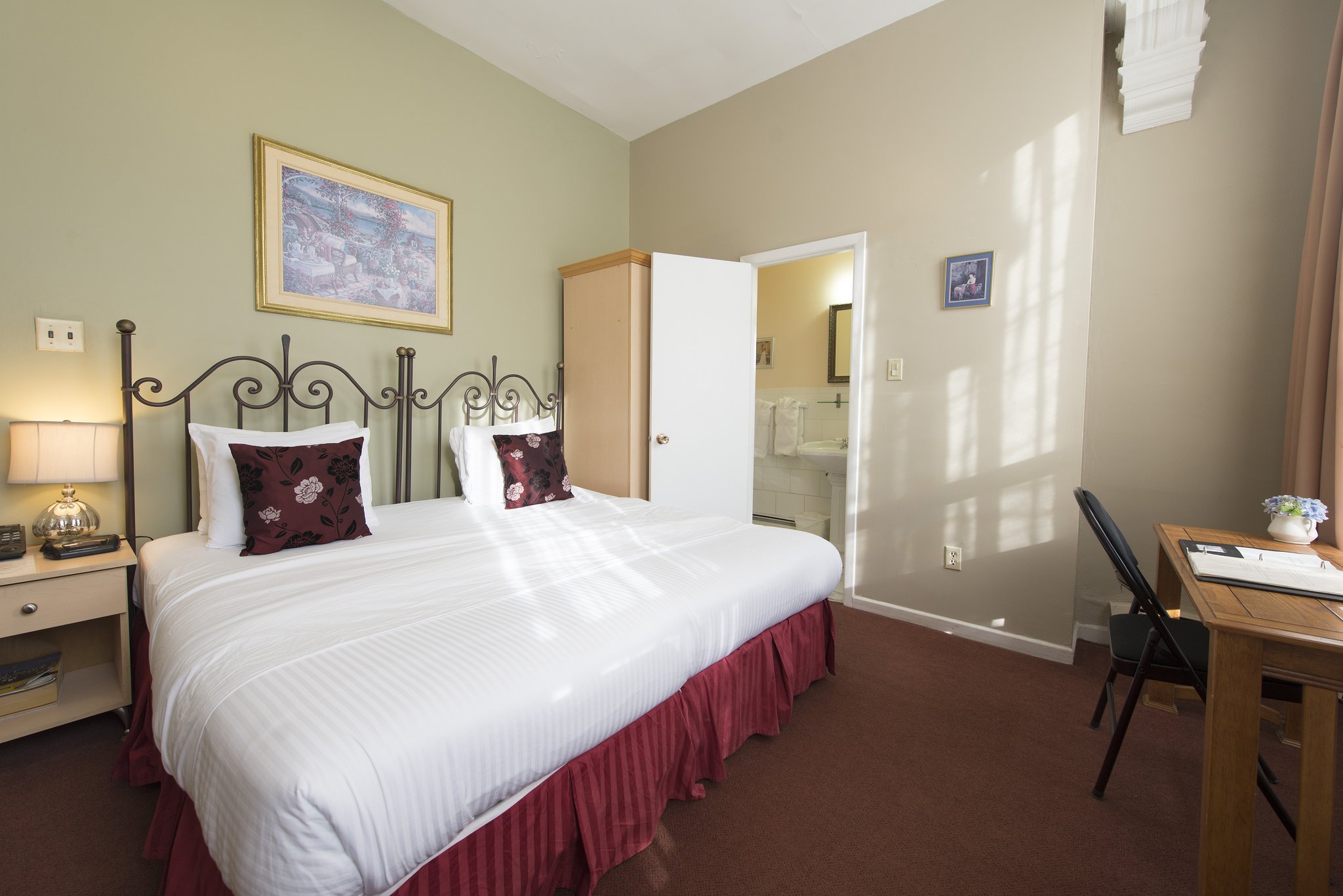 A bright guest room with a king bed, a nightstand, and a work desk