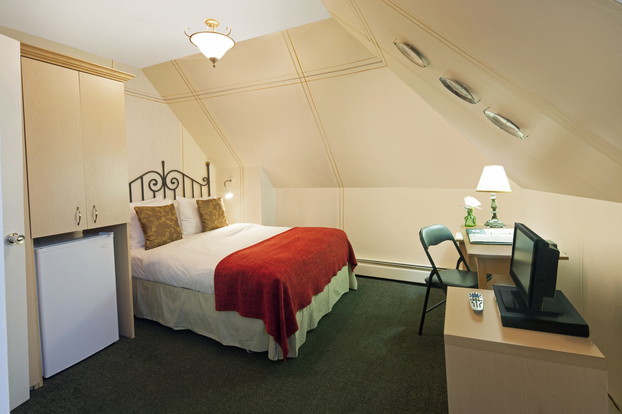A bright guest room with a double bed, a desk, and a small TV