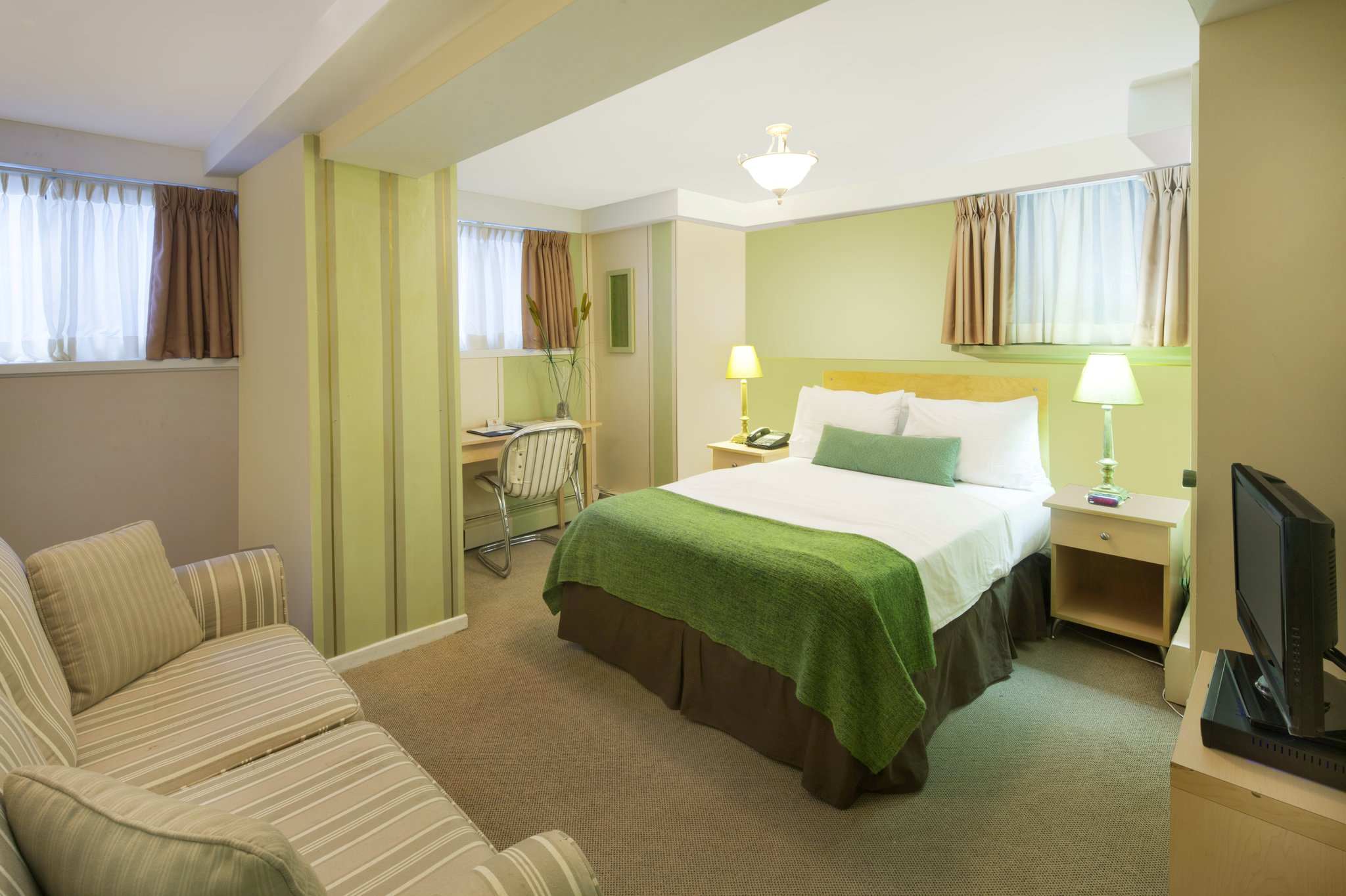 A studio guest room with one double bed, a sofa, and a TV